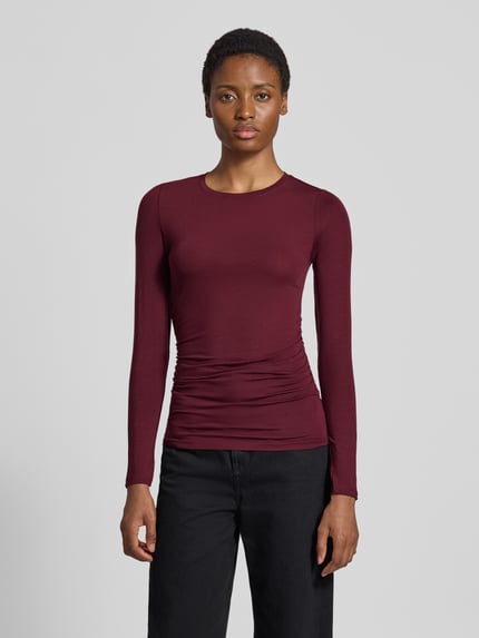 Frauenmodel trägt Slim Fit Langarmshirt aus Lyocell-Mix Modell 'AVA' von VERO MODA in Dunkelrot, feine Struktur, schlichtes Design, Ganzkörperansicht von vorne. Damen Langarmshirt von VERO MODA.