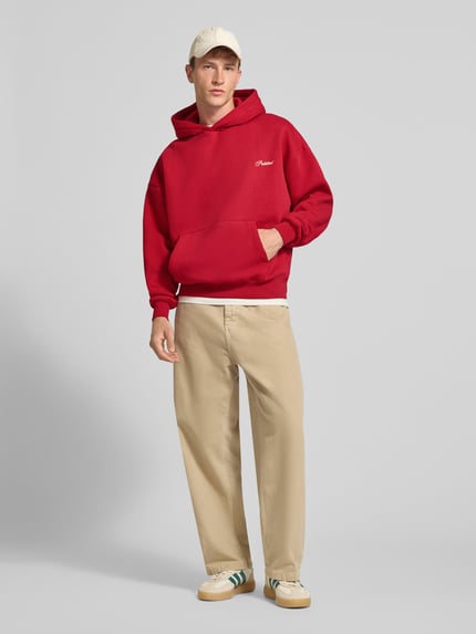 Männermodel trägt Relaxed Fit Hoodie aus Baumwoll-Mix mit Label-Stitching von PROHIBITED in Rot, Känguru-Tasche, Ganzkörperansicht von vorne.