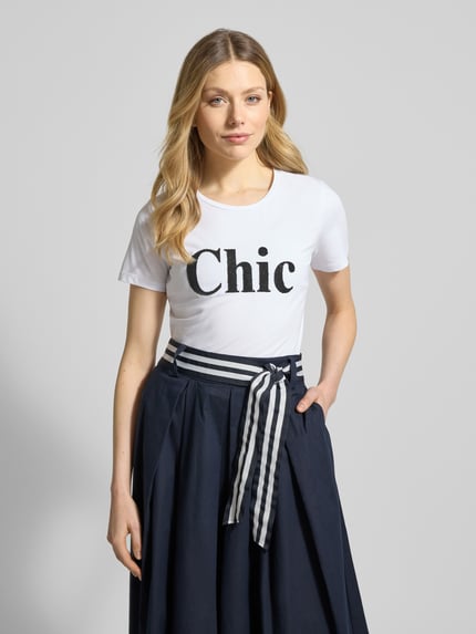 Frauenmodel trägt T-Shirt mit Rundhalsausschnitt und Perlen von More & More, Weiß mit Statement-Print, regular Fit, Nahaufnahme Oberkörper.