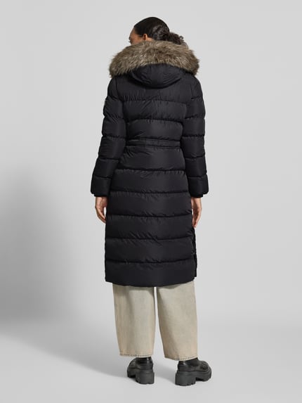 Frauenmodel trägt Steppmantel mit Pattentaschen von Superdry, schwarze Farbe, Kapuze mit Kunstfell, Rückenansicht, Ganzkörperansicht von hinten.