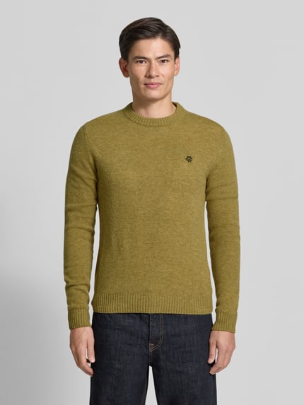 Männermodel trägt Slim Fit Strickpullover aus reiner Wolle mit Label-Stitching von MCNEAL, olivgrün, gerippte Abschlüsse, Ganzkörperansicht von vorne.