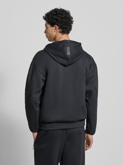 Männermodel trägt schwarze Sweatjacke mit Kapuze von adidas Sportswear, Regular Fit, Label-Print, Material-Mix, Ganzkörperansicht Rückansicht.