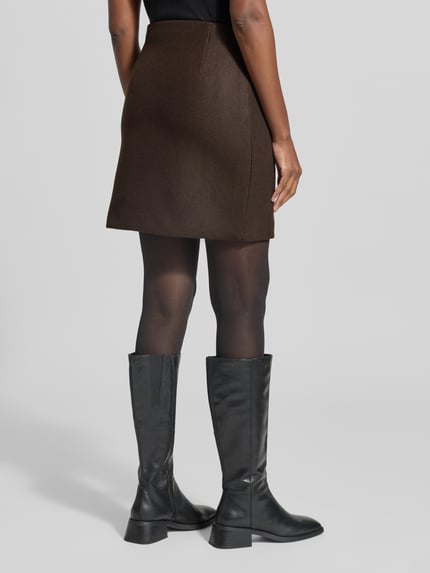 Frauenmodel trägt Ausgestellter Mini-Rock mit Nahtreißverschluss Modell 'FORTUNEALLISON' von VERO MODA in Dunkelbraun, Damen Mini-Rock, Ganzkörperansicht Rückansicht.
