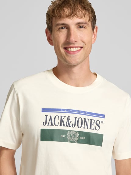 Męski model nosi t-shirt z nadrukiem z logo, Model 'FREDERIKSBERG' od JACK & JONES, bawełna, prosty krój, okrągły dekolt, długość tyłu w rozmiarze M: 70 cm, zbliżenie na górną część ciała.