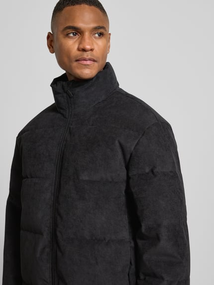 Mannenmodel draagt Regular Fit Gewatteerd jack uit corduroy van Tom Tailor Denim in effen zwart met opstaande kraag, nahaufnahme bovenlichaam.