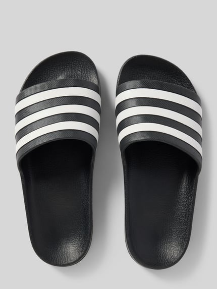 Produktfoto, Badeschuhe mit Kontraststreifen Modell 'ADILETTE AQUA' von adidas, schwarz mit weißen Streifen, strukturierte Sohle, Allover-Muster, flache Absatzform, abgerundete Schuhspitze, Schlupfvariante, Damen Badeschuhe