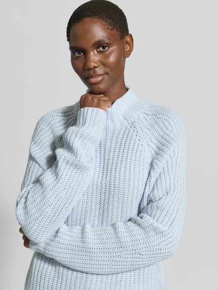 Frauenmodel trägt Strickpullover aus Kaschmir-Baumwoll-Mix Modell 'LONA' von 0039 Italy in Hellblau, grobe Rippstruktur, Nahaufnahme Oberkörper. Regular Fit, Stehkragen, weiche Textur, Damenpullover, Rückenlänge 60 cm, Ärmellänge 78 cm.