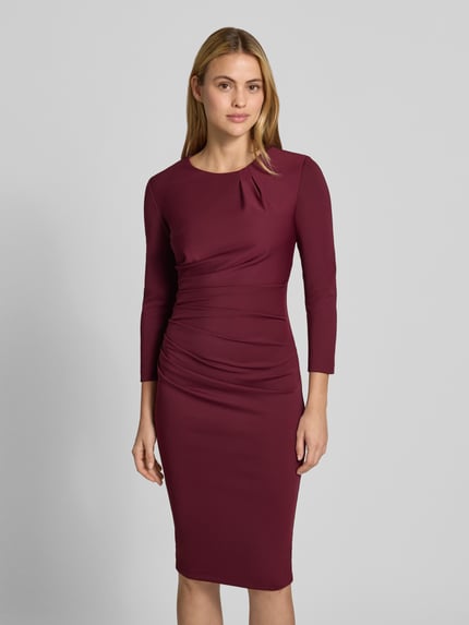 Frauenmodel trägt Cocktailkleid mit Raffungen von Rinascimento in Bordeaux, Langarm, knieumspielend, Material-Mix, Ganzkörperansicht von vorne.