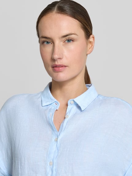 Vrouwenmodel draagt lichtblauwe linnen blouse met knoopsluiting model 'DOLLY' van 0039 Italy, regular fit, overhemdkraag, omslag aan mouwen, ruglengte bij maat S 64 cm, detailopname bovenlichaam.