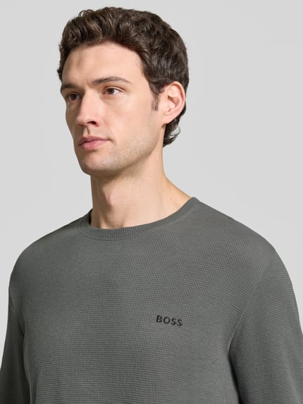 Männermodel trägt Longsleeve mit Logo-Schriftzug von BOSS, unifarbene Optik, Rundhals, langarm, Nahaufnahme Oberkörper.