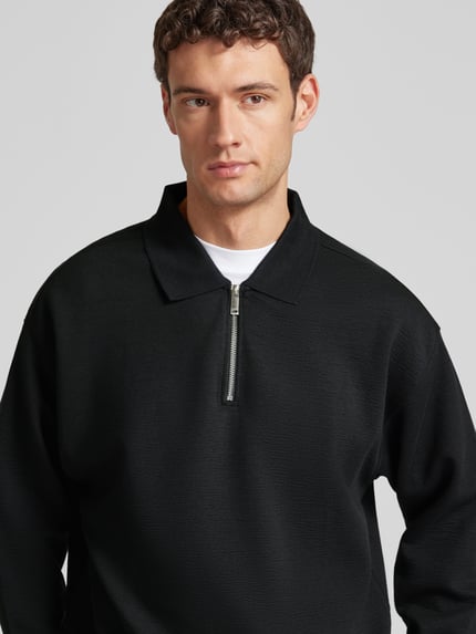 Männermodel trägt Sweatshirt mit Polokragen und Reißverschluss von CK Calvin Klein aus Material-Mix mit Modal-Anteil, Strukturmuster, Relaxed-Fit, Nahaufnahme Oberkörper.