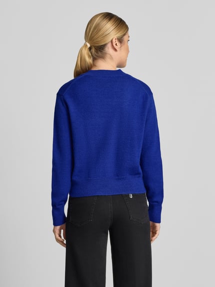 Frauenmodel trägt Strickpullover mit V-Ausschnitt Modell 'LIMONI' von MANGO in kräftigem Blau, glatte Textur, Rückenansicht, Regular Fit, elastische Abschlüsse, Rückenlänge 52 cm, Ärmellänge 58 cm.