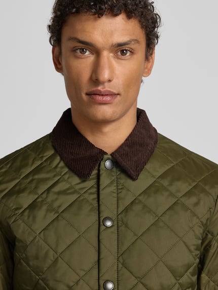 Männermodel trägt Steppjacke mit Umlegekragen von Barbour, Unifarbenes-Design, Druckknopfleiste, Label-Stitching, Nahaufnahme Oberkörper.