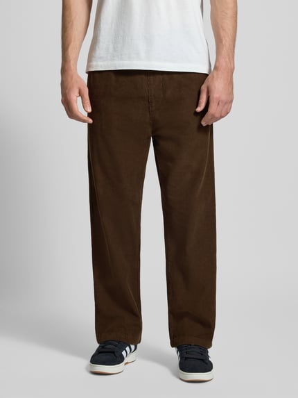 Männermodel draagt Stoffhose met elastische band van Pegador in bruin, puur katoen, los model, steekzakken, labelstitching, binnenbeenlengte 62 cm, bandwijdte 65 cm, voorkant, detailopname.
