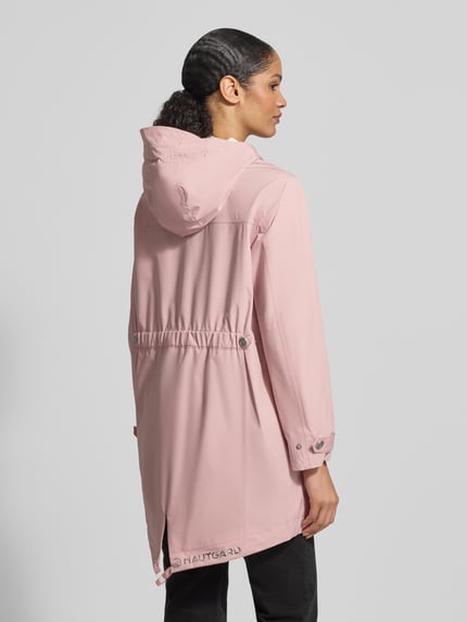 Modelka kobieca ma na sobie różową Jacke mit Ärmelriegeln od NAUTGÅRD, krój regular fit, kaptur z troczkiem, kieszenie na zamek, długość tyłu w rozmiarze S: 90 cm, szerokość ramion w rozmiarze S: 45 cm, szerokość klatki piersiowej w rozmiarze S: 51 cm, długość rękawa w rozmiarze S: 62 cm, widok całej sylwetki z tyłu.