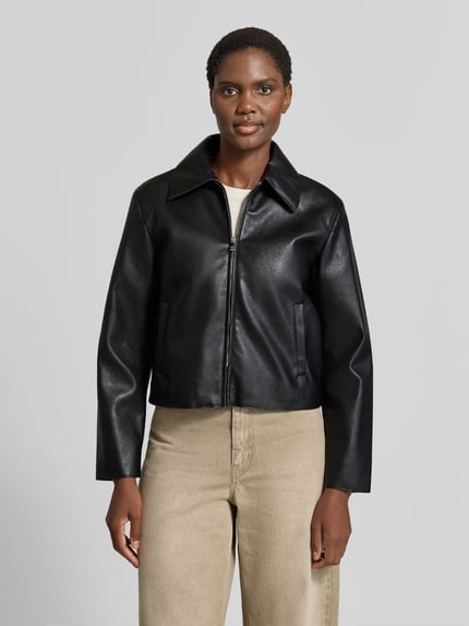 Frauenmodel trägt schwarze Jacke in Leder-Optik Modell 'SABINA' von MANGO, gerade Passform, Umlegekragen, Ganzkörperansicht von vorne.