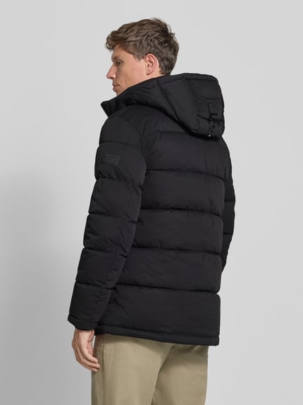 Männermodel trägt schwarze Steppjacke mit Brusttasche von S.OLIVER CASUAL, unifarben, Struktur, Longline, Label-Detail, Ganzkörperansicht Rückansicht.