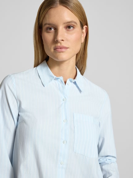 Frauenmodel trägt Regular Fit Hemdbluse mit Brusttasche Modell 'Darma' von Vila aus Baumwoll-Mix, hellblau-weiß gestreift, Nahaufnahme Oberkörper.