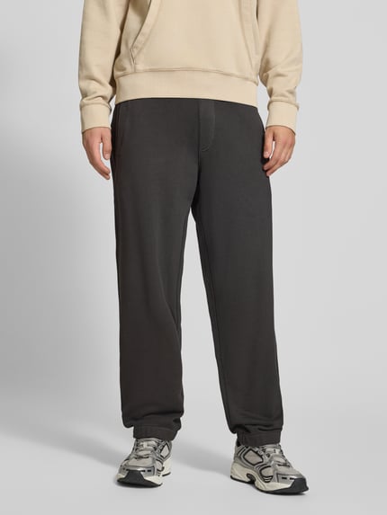 Männermodel trägt Relaxed Fit Sweathose aus reiner Baumwolle von G-Star RAW in Dunkelgrau mit elastischen Bündchen, Nahaufnahme Unterkörper.
