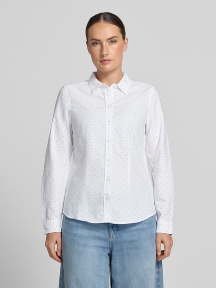Frauenmodel trägt Bluse mit Hemdblusenkragen und Knopfleiste von Christian Berg Woman, reine Baumwolle, weiß mit feinem Punktmuster, leicht taillierter Schnitt, abgerundeter Saum, Ganzkörperansicht von vorne.