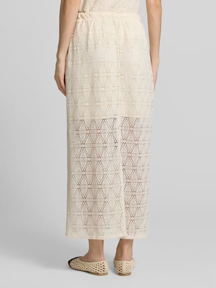 Frauenmodel trägt Leicht ausgestellter Midi-Rock aus Spitze mit elastischem Bund Modell 'MAYA' von Vero Moda, cremefarben mit geometrischer Spitzenstruktur, unifarben, mittellang, transparenter Spitzensaum mit blickdichtem Unterrock, Gehschlitz und elastischer Bund, Ganzkörperansicht Rückansicht.