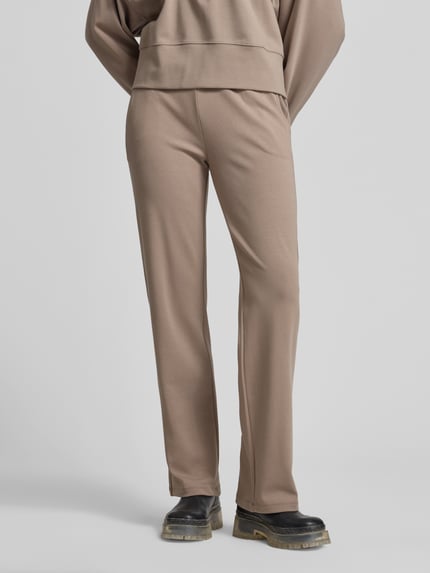 Frauenmodel trägt Flared Fit Sweatpants mit Tunnelzug von Juvia in Beige, aus elastischem Baumwoll-Modal-Mix, mit Eingrifftaschen, Ganzkörperansicht von vorne.