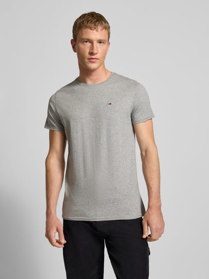 Männermodel trägt T-Shirt in Melange-Optik von Tommy Jeans aus reiner Baumwolle, graue Farbe, gerader Schnitt, Ganzkörperansicht von vorne.