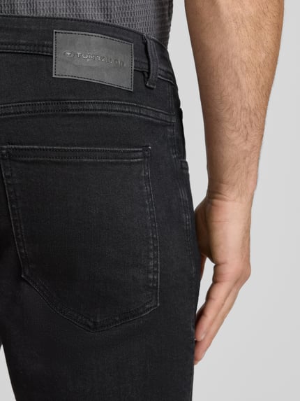 Männermodel trägt Regular Fit Jeans Bermudas aus Baumwoll-Mix von Tom Tailor, schwarze Denim, Label Patch, Nahaufnahme Rückansicht.