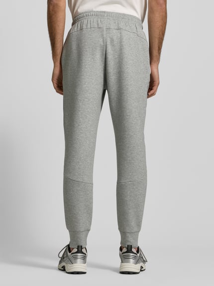Männermodel trägt Regular Fit Sweatpants mit Logo-Print Modell 'Unstoppable' von Under Armour in lichtgrijs met elastische tailleband en boorden, ritszak aan de pijp, katoenmengsel, regular fit, volledige lichaamsopname achterkant.