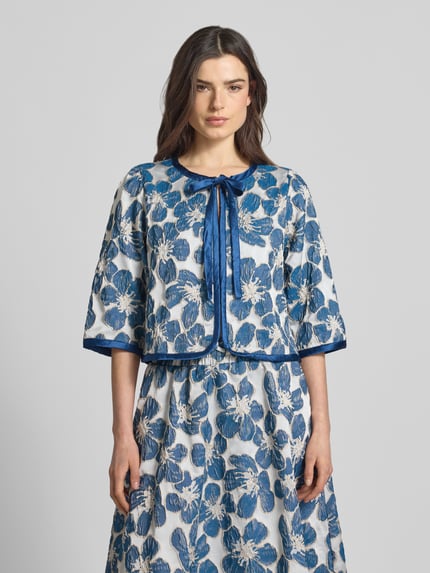 Kobiece model prezentuje kurtkę z mieszanki materiałów z dodatkiem streczu, krój regular fit, model 'Trine' od LOLLYS LAUNDRY, wiązanie, rękaw o dł. 3/4, długość tyłu w rozmiarze S 49 cm, szerokość ramion w rozmiarze S 36 cm, szerokość w rozmiarze S 49 cm, długość rękawów w rozmiarze S 44 cm, niebieski wzór kwiatowy, widok całego ciała z przodu.