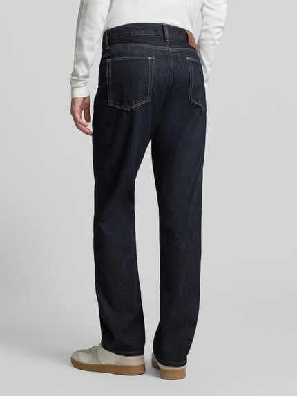 Männermodel trägt Straight Fit Jeans aus reiner Baumwolle von Tommy Hilfiger in dunklem Denim mit Label Patch und Gürtelschlaufen, Ganzkörperansicht Rückansicht.