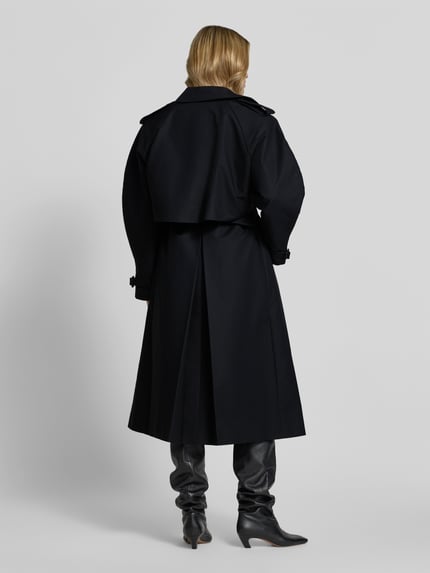 Frauenmodel trägt schwarzen Trenchcoat aus reiner Baumwolle von Anine Bing, taillierte Passform, Rückansicht, Ganzkörperansicht.