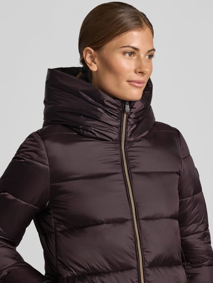 Frauenmodel trägt Steppmantel mit Kapuze Modell 'LYSA' von Save The Duck in Dunkelviolett, glatte Struktur, Nahaufnahme Oberkörper. Gerader Schnitt, Zweiwege-Reißverschluss, Label-Patch, seitliche Eingrifftaschen, Kontext: Damen Steppmantel Save The Duck.