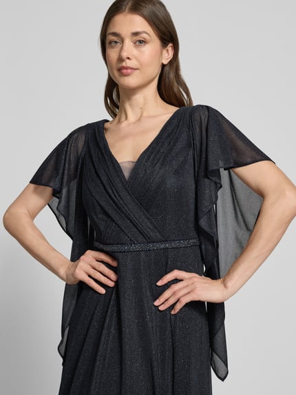 Frauenmodel trägt Maxikleid mit V-Ausschnitt und Ziersteinbesatz von Vera Mont in Glitzer-Optik, taillierte Passform, Volantärmel, Falten-Optik, Farbe Dunkelblau, texturierte Oberfläche; Rückenlänge bei Größe 38: 133 cm, Brustweite: 42 cm, Ärmellänge: 24 cm. Nahaufnahme Oberkörper.