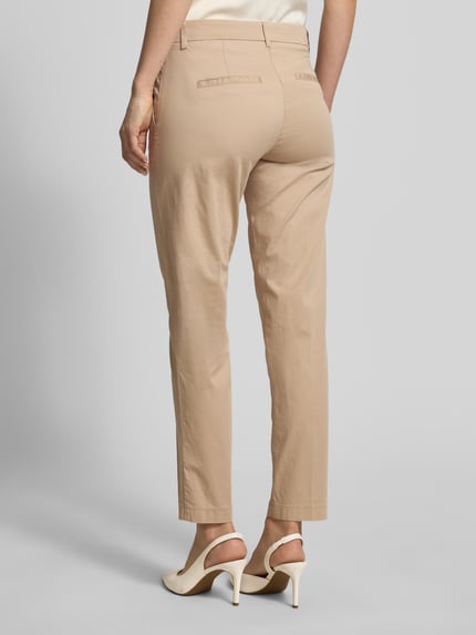 Frauenmodel trägt Hose in verkürzter Passform Modell 'MARON' von Brax aus beige Baumwoll-Mix mit Lyocell, Ganzkörperansicht Rückansicht.