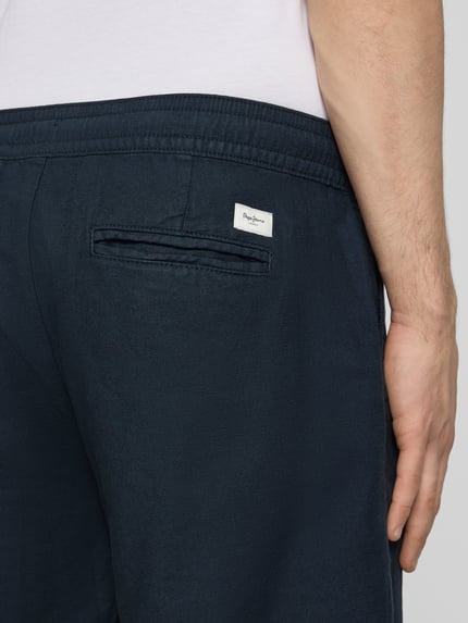 Mężczyzna nosi Relaxed Fit Chinoshorts aus Baumwoll-Leinen-Mix od Pepe Jeans, granatowy kolor, widoczna tylna kieszeń i label patch, tekstura bawełniano-lniana, ujęcie detailaufnahme tylnej części.