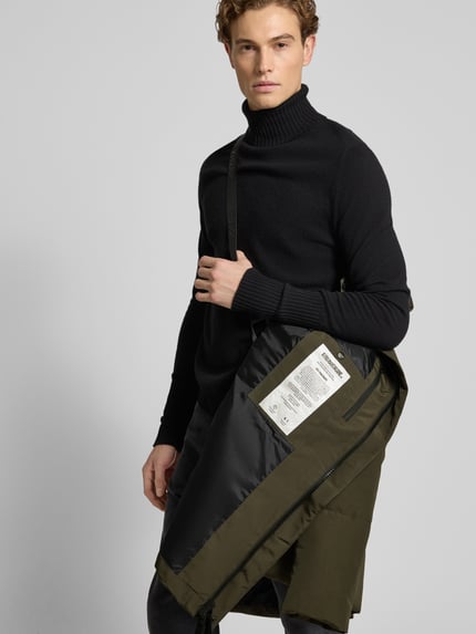 Männermodel trägt Regular Fit Steppmantel mit Logo-Patch Modell 'Zeno' von khujo in Dunkelgrün, Stepp-Optik, Detailaufnahme Oberkörper. Rückenlänge 88 cm, Schulterbreite 49 cm, Brustweite 61 cm, Ärmellänge 67 cm, elastische Ärmelabschlüsse, Kapuze mit Tunnelzug, durchgehende Abdeckleiste.