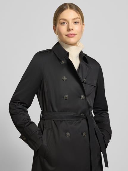 Modelka kobieca nosi Regular Fit płaszcz z wykładanym kołnierzem Fuchs Schmitt, mieszanka bawełny, listwa guzikowa 2-rzędowa, taliowany krój, odpinana materiałowa tasiemka, czarny kolor, gładka tekstura, widok całej sylwetki z przodu.