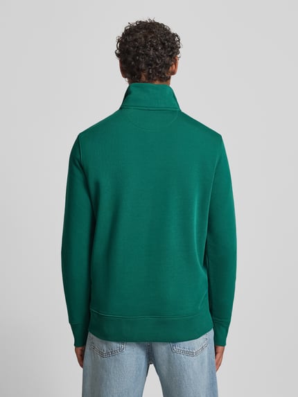 Męski model nosi Bluza z stójką i zamkiem błyskawicznym od Gant, mieszanka bawełny, krój regular fit, zielona, wyhaftowane logo, długość tyłu 72 cm, długość rękawów 65 cm, widok całej sylwetki z tyłu.