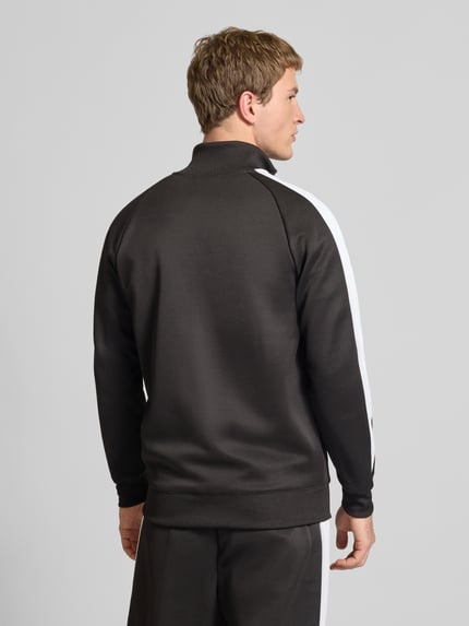 Męski model ma na sobie Sweatjacke mit Label-Print od PUMA PERFORMANCE, czarno-biały, materiał z bawełną, krój regular fit, stójka, prążkowane wykończenia, zamek, kieszenie na zamek, nadruk z logo, długość pleców w rozmiarze M: 73 cm, długość rękawa w rozmiarze M: 52 cm, widok całej sylwetki z tyłu.