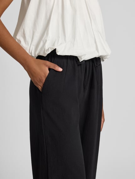 Frauenmodel trägt schwarze Stoffhose in verkürzter Passform Modell 'CISSIE' von Soyaconcept aus reiner Baumwolle mit Tunnelzug, Nahaufnahme Oberkörper.