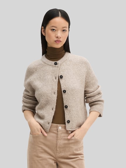 Frauenmodel trägt Strickjacke aus Alpaka Wolle mit Rollsaum von Marc O'Polo in Melange-Strickoptik, Struktur, Knopfleiste, Nahaufnahme Oberkörper.
