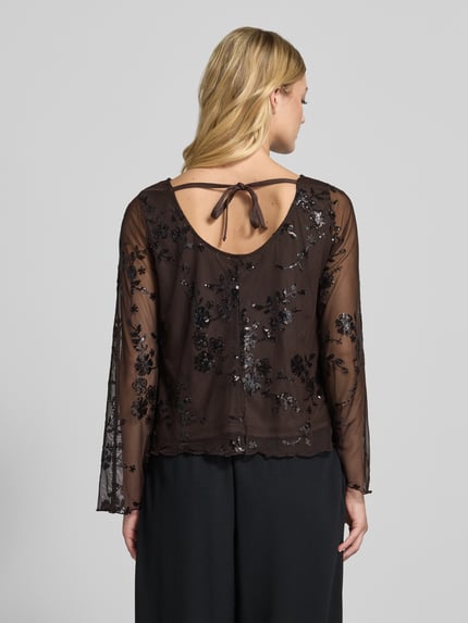 Frauenmodel trägt Kurz Langarmbluse mit Paillettenapplikation von PIECES, florales Spitzenmuster, brauner Chiffon, Ganzkörperansicht Rückansicht.