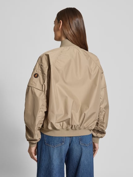 Frauenmodel trägt Bomberjacke mit Reißverschlusstaschen Modell 'LIL' von SAVE THE DUCK in Beige, Material-Mix mit Stretch-Anteil, Regular-Fit, Stehkragen und Reißverschluss, Ganzkörperansicht Rückansicht. Kontext: Rückenlänge bei Größe S 53 cm, Schulterbreite 42 cm, Brustweite 61 cm, Ärmellänge 70 cm.