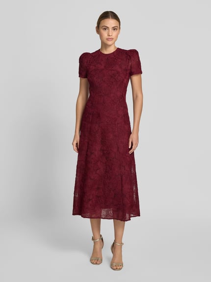 Frauenmodel trägt Maxikleid mit floralem Allover-Besatz von ROTATE aus Elastischer-Material-Mix, taillierte Passform, Rundhalsausschnitt, kurzärmelig, bordeauxrot, strukturierte Oberfläche, Gesamtlänge 133 cm, Brustweite 45 cm, Ärmellänge 22 cm, Ganzkörperansicht von vorne.