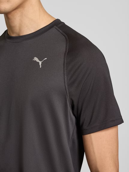Mężczyzna nosi T-Shirt mit Logo und Rundhalsausschnitt von PUMA PERFORMANCE, czarny, krój regular fit, logo, długość tyłu w rozmiarze M 70 cm, zbliżenie na górną część ciała
