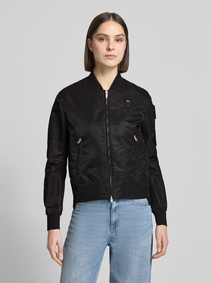 Frauenmodel trägt Bomberjacke mit Reißverschlusstaschen Modell 'LAURIE' von Blauer Usa in Schwarz, gerippte Abschlüsse, Ganzkörperansicht von vorne. Rückenlänge bei Größe S: 57 cm, Schulterbreite: 44 cm, Brustweite: 43 cm, Ärmellänge: 62 cm.