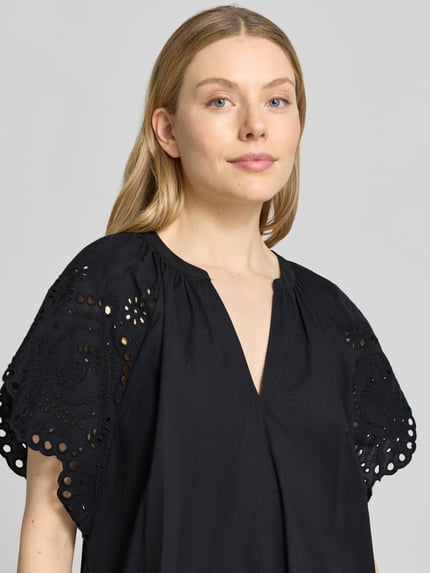 Frauenmodel trägt Relaxed Fit Minikleid mit floraler Lochstickerei von Christian Berg Woman Selection in Schwarz, reine Baumwolle, Tunika-Ausschnitt, kurzärmelig, Nahaufnahme Oberkörper.