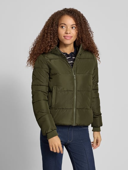 Frauenmodel trägt grüne Steppjacke mit Kapuze von PIECES, strukturierte Webware, seitliche Taschen, Reißverschluss, Ganzkörperansicht von vorne.