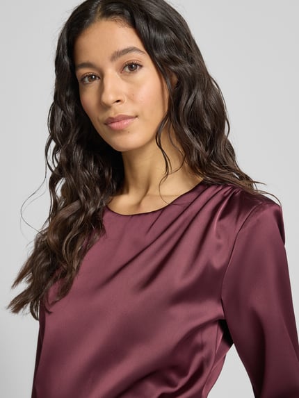 Frauenmodel trägt knielanges Cocktailkleid mit Rundhalsausschnitt von Rinascimento aus Satin in dunklem Violett, körpernahe Passform, Nahaufnahme Oberkörper.